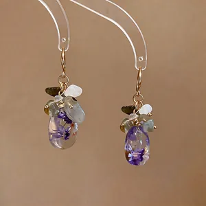 Detail view of handmade translucent resin earrings with dried purple flowers and stones.