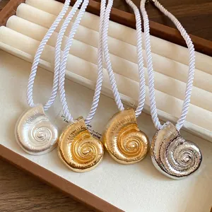 Elegant metallic shell pendant necklaces with white silk ropes on a display tray.