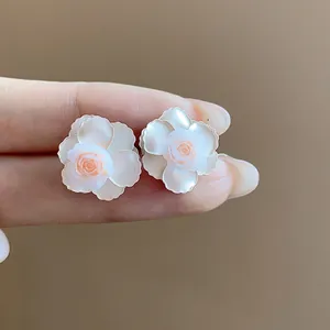 Gros plan d'élégantes boucles d'oreilles fleurs en résine blanc crème et rose en main