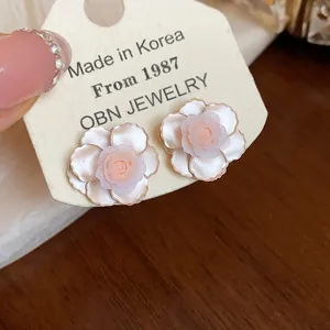 Vue détaillée de boucles d'oreilles élégantes camélia en résine rose sur carte crème