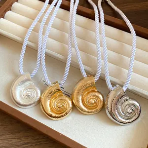 Detailed view of four sea shell pendant necklaces with white twisted silk ropes in jewelry tray.