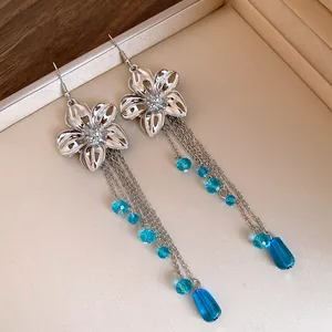 Dettaglio di orecchini a fiore d'argento con nappe di cristallo blu e gocce.