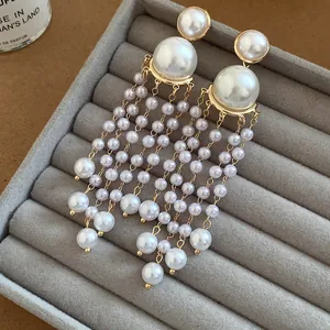 Detailed view of elegant long pearl tassel earrings on a grey velvet tray.