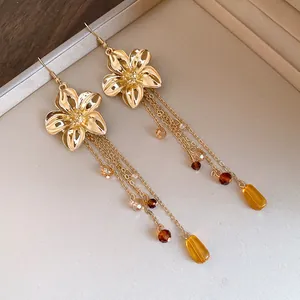 Dettaglio ravvicinato di orecchini a fiore dorati con eleganti nappe di cristallo ambra