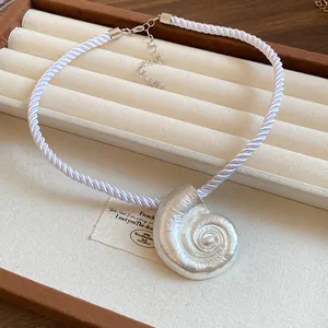 Detailed view of silver metallic seashell pendant on a white silky cord necklace.