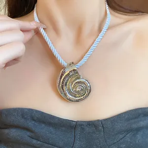 Detailed close-up of a metallic silver snail pendant on a white twisted silk rope chain necklace