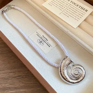 Detailed view of silver seashell pendant with white twisted rope chain in jewelry box