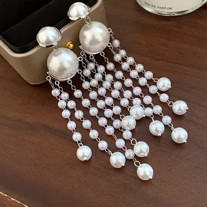 Close-up detail of elegant long pearl tassel earrings displayed on a dark wooden background
