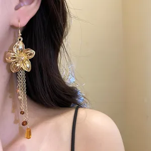 Dettaglio di orecchini a fiore in oro con eleganti nappe e perle d'ambra sul modello