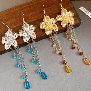 Dettaglio di orecchini a fiore con lunghe nappe di perline color oro e argento lucido