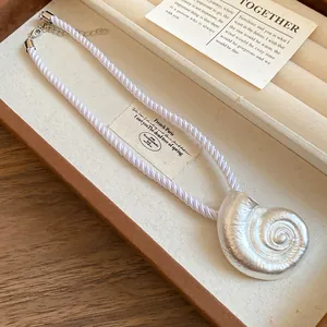 Close-up of white mercerized rope necklace with a textured silver conch pendant