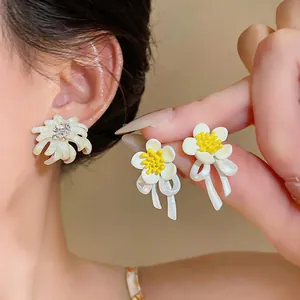 Detailed macro view showing delicate white flower earrings with yellow centers and ribbon design
