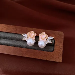 Close-up of vintage pink enamel flower earrings with pearls and CZ on a wooden stand.