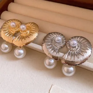 Elegant gold and silver shell earrings with pearl pendants displayed in jewelry tray