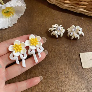 Close-up of elegant white flower earrings with yellow center and ribbon detail.