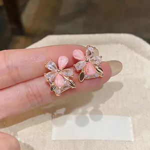 Exquisite close-up of pink flower stud earrings with sparkling crystals shown on finger