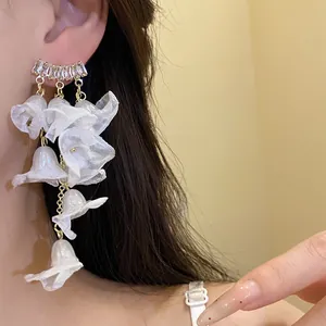 Close-up detail of white chiffon flower tassel earrings with zircon studs on ear.