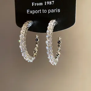Close-up detail of exquisite C-shaped silver hoop earrings encrusted with sparkling zirconia.