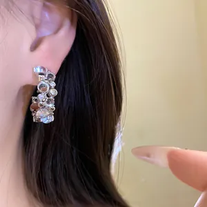 Detail view of elegant C-shaped silver earrings with sparkling zircon resin clusters on ear