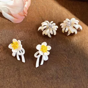 Detailed view showing two pairs of white and cream enamel flower stud earrings on wood