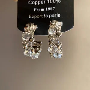 Detailed close-up of C-shaped earrings with clear resin beads and sparkling zircons