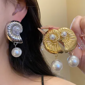 Close-up detail of stylish gold and silver conch shell earrings with pearl drops