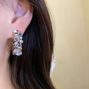 Close-up of elegant C-shaped ear studs with zircon and resin on a female model's ear.
