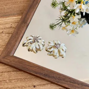 Close-up detail of white enamel flower stud earrings with shimmering glitter and rhinestones.