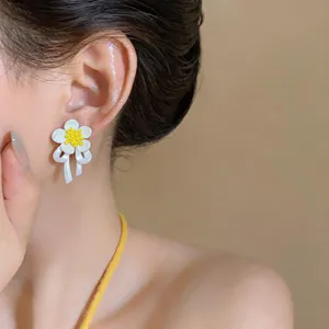 Close-up of white flower earrings with yellow center and ribbon detail on model