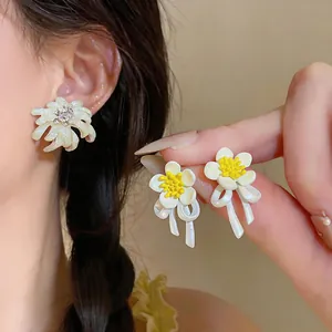 Detail macro view of elegant white oil-dripped flower earrings with yellow centers and ribbons