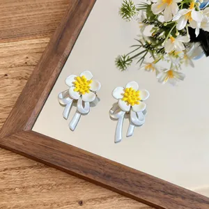 Detailed view of white flower stud earrings with elegant bow accents on a mirror surface.