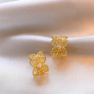 Primer plano de elegantes pendientes dorados en forma de C con diseño floral y circón.