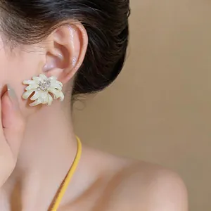 Close-up of elegant cream enamel flower stud earring with rhinestone center