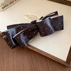Détail d'une pince à cheveux vintage à nœud en satin noir avec des pois blancs.