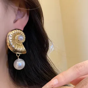 Close-up of elegant gold nautilus seashell earrings with pearl drops worn by model
