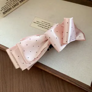 Gros plan d'une pince à cheveux nœud en satin rose à pois noirs sur fond.