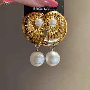 Elegant close-up of golden sea shell dangle earrings with large white pearl accents