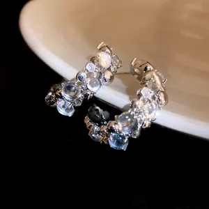 Close-up of C-shaped stud earrings with zircon and resin beads on a white surface