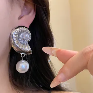 Detailed close-up showing a silver metal conch-shaped earring with a white pearl pendant