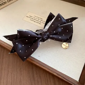 Gros plan de la pince à cheveux en satin noir à pois vintage avec breloque dorée
