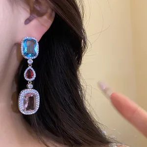 Close-up of elegant dangling zircon earrings with blue red and pink stones