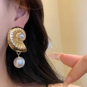 Detailed close-up showing an elegant gold conch shell earring with a white pearl drop