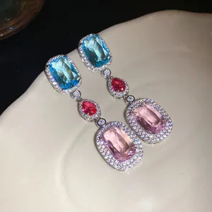 Detail of elegant drop earrings with blue, red, and pink zircons in a light luxury design
