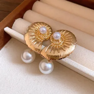 Close-up detail of golden conch shell earrings with elegant pearl pendants