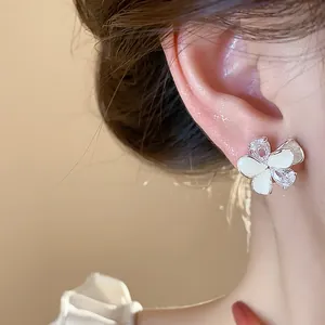 Close-up of elegant flower stud earring with white enamel and sparkling zircons.