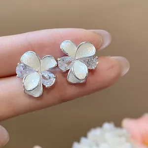 Detailed close-up of sparkly silver flower stud earrings with zircon and white oil-dripping