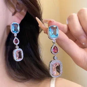Close-up of elegant three-tier zircon drop earrings with blue, red, and pink gemstones