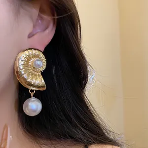 Detailed macro view of a golden conch-shaped earring with a white pearl drop on ear