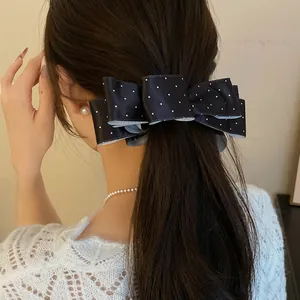 Gros plan d'une pince à cheveux vintage à pois en satin noir sur cheveux ondulés