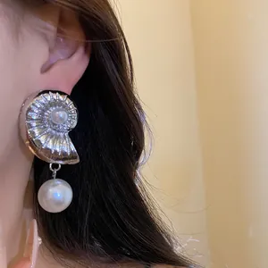 Detailed view of a silver conch shell earring with elegant pearl accents on a model